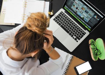 Overhead view of a stressed woman working at a desk with a laptop, phone, and notebooks.