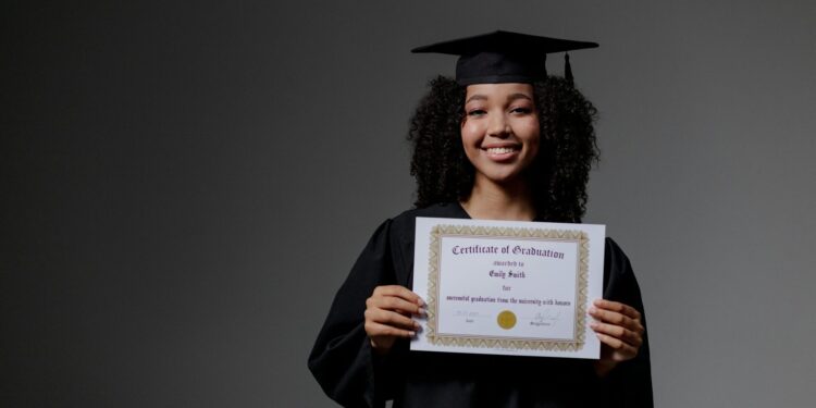 Smiling graduate proudly holding a certificate in cap and gown.
