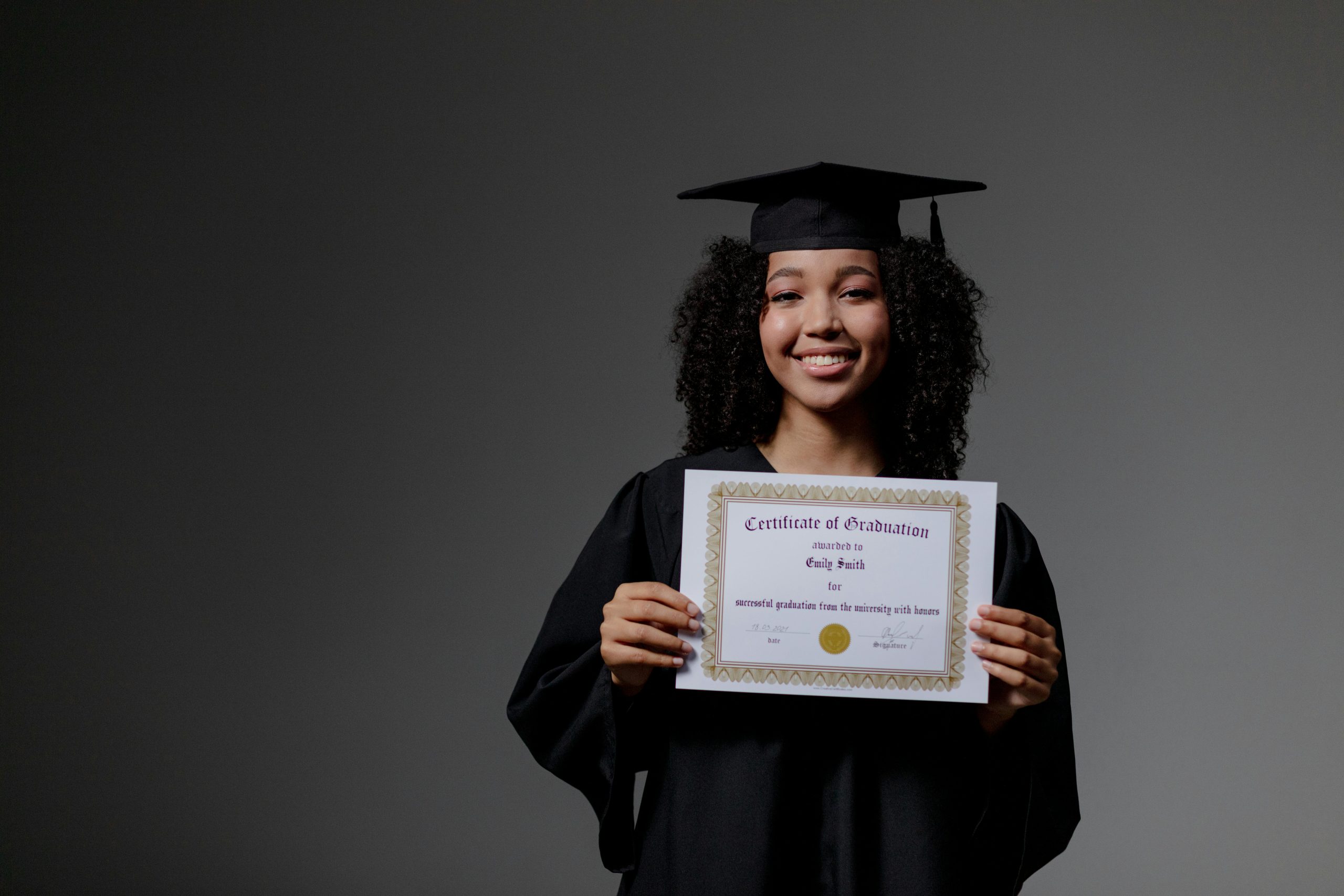 Smiling graduate proudly holding a certificate in cap and gown.