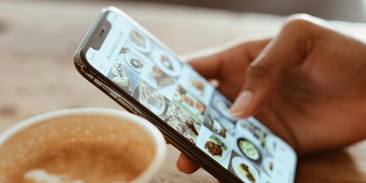 Hand browsing social media photos on a smartphone next to a cup of coffee indoors.