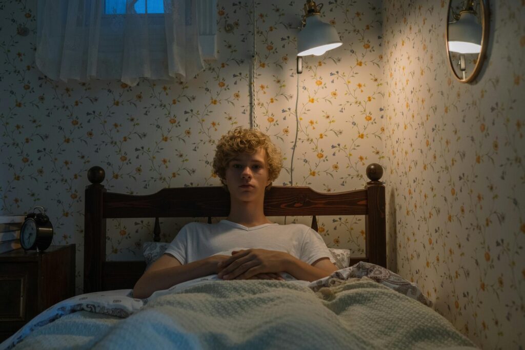 Teenager lying in bed with vintage decor and warm lighting, creating a cozy atmosphere.