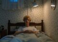 Teenager lying in bed with vintage decor and warm lighting, creating a cozy atmosphere.