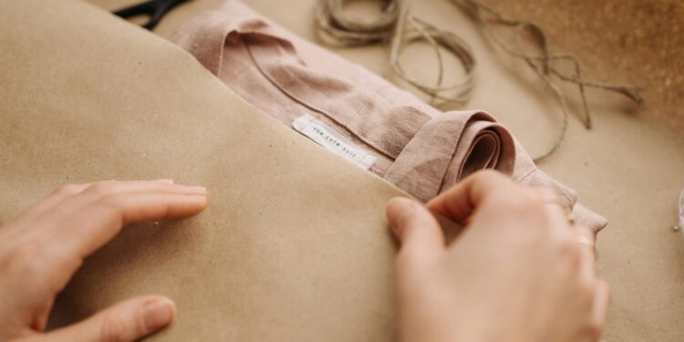 Close-up of hands wrapping a linen shirt with twine, showcasing craftsmanship and sustainable fashion.