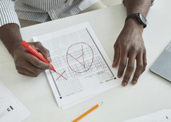Close-up of a teacher marking a test paper with a red marker on a desk.