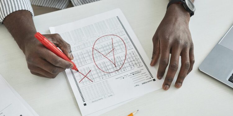 Close-up of a teacher marking a test paper with a red marker on a desk.