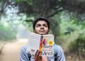 A young man relaxes while reading 'Power of Your Subconscious Mind' outdoors in a park.