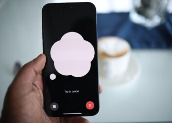 Close-up of a smartphone in hand with AI voice chat bubble and coffee in background.