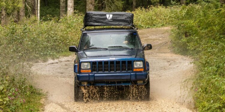 A rugged 4x4 vehicle navigates through muddy trails in the Asiago forests of Italy, showcasing adventure and nature.