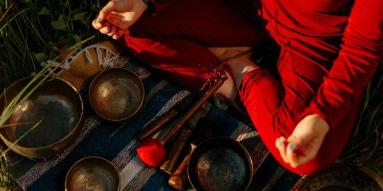 A person meditating outdoors with Tibetan singing bowls, creating a peaceful atmosphere.