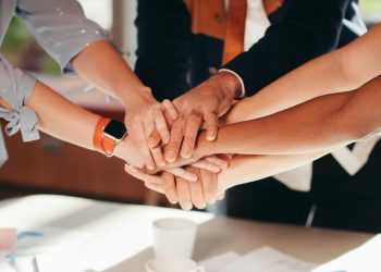 A close-up shot of diverse team members stacking hands over a white table, symbolizing unity and collaboration.