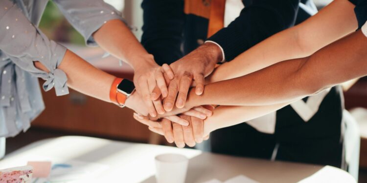 A close-up shot of diverse team members stacking hands over a white table, symbolizing unity and collaboration.