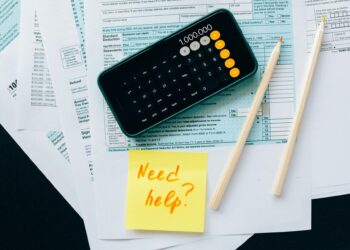 Top view of financial papers with a calculator, pencils, and a note saying 'Need help?' indicating tax or accounting assistance.