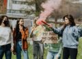 Group of women at a protest for women's rights holding signs and lighting a smoke bomb outdoors.