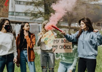 Group of women at a protest for women's rights holding signs and lighting a smoke bomb outdoors.