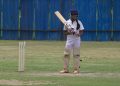A young female cricket player poised to bat on a grassy field in Gahunje, India.