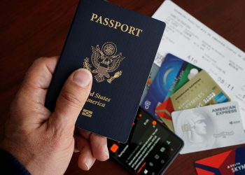 A close-up of a US passport with credit cards, tickets, and a mobile phone on a table.