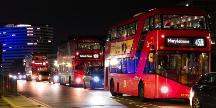 Red double-decker buses in London's nighttime traffic, showcasing urban life.