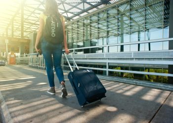 A woman walks with a suitcase outside an airport terminal, ready for travel.
