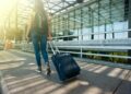 A woman walks with a suitcase outside an airport terminal, ready for travel.