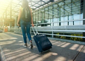 A woman walks with a suitcase outside an airport terminal, ready for travel.