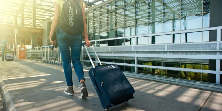 A woman walks with a suitcase outside an airport terminal, ready for travel.