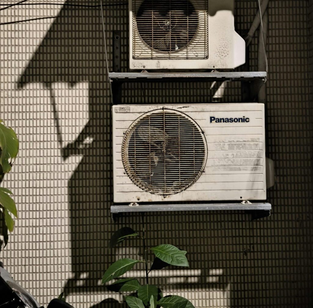 Close-up of two air conditioning units on a building facade in sunlight.