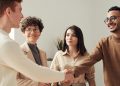 Four colleagues in an office handshake demonstrating teamwork and cooperation.