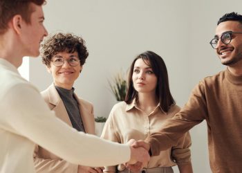 Four colleagues in an office handshake demonstrating teamwork and cooperation.