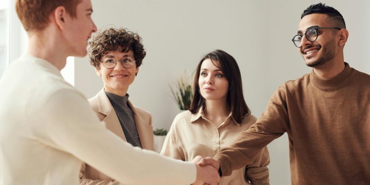 Four colleagues in an office handshake demonstrating teamwork and cooperation.