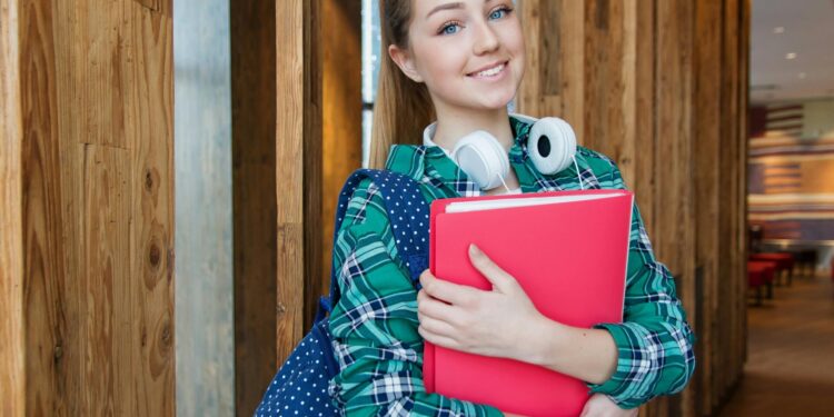 Smiling student holding book and wearing headphones, ready for study.