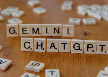 Close-up of wooden Scrabble tiles spelling Gemini and ChatGPT on a wooden surface.