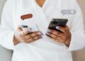 A woman in a white robe interacts with two smartphones, showcasing social media engagement icons.