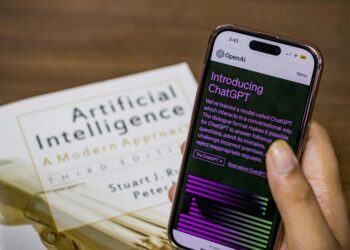 Close-up of a smartphone displaying ChatGPT app held over AI textbook.
