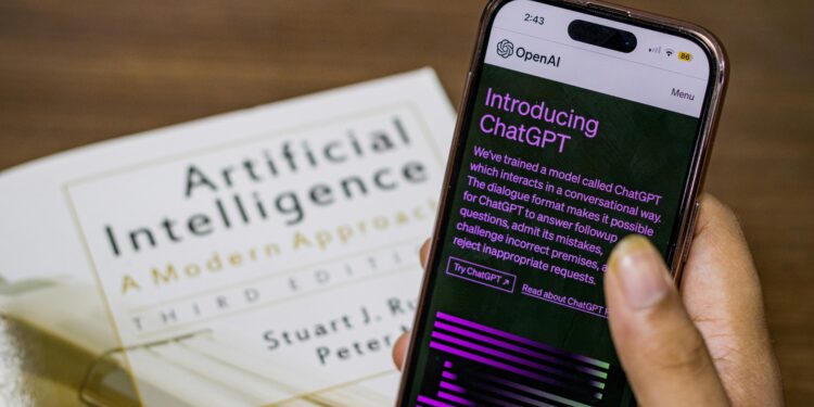 Close-up of a smartphone displaying ChatGPT app held over AI textbook.