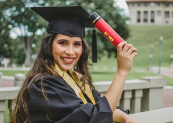 Young woman in graduation cap and gown celebrating with diploma outdoors.