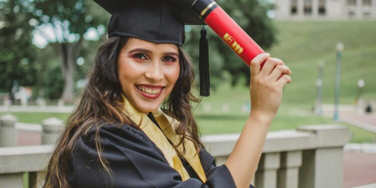 Young woman in graduation cap and gown celebrating with diploma outdoors.