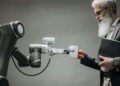 An elderly man receives a cup from a robotic arm in a modern office setting.
