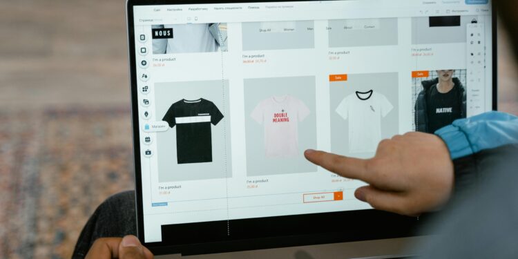 A person points to t-shirt options in an online store on a laptop screen.