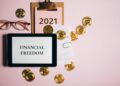 Flat lay image of financial freedom concept with bitcoins, tablet, and clipboard on a pink background.