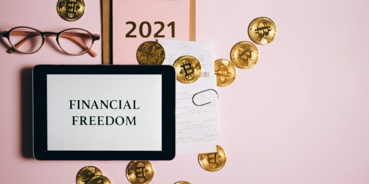 Flat lay image of financial freedom concept with bitcoins, tablet, and clipboard on a pink background.