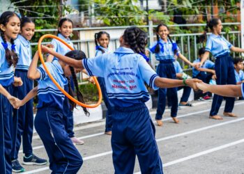 Group of schoolchildren enjoying outdoor games with hula hoops at a school event in Surat, India.