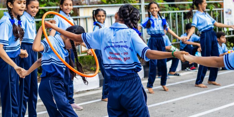 Group of schoolchildren enjoying outdoor games with hula hoops at a school event in Surat, India.