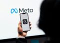 Hands holding smartphone with Meta Threads logo on screen, Meta branding in background.