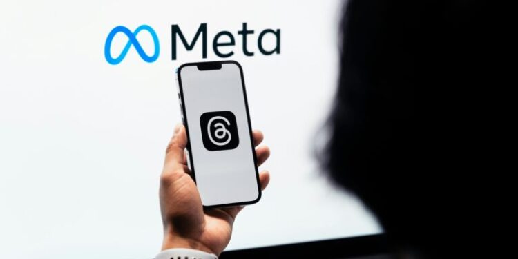 Hands holding smartphone with Meta Threads logo on screen, Meta branding in background.