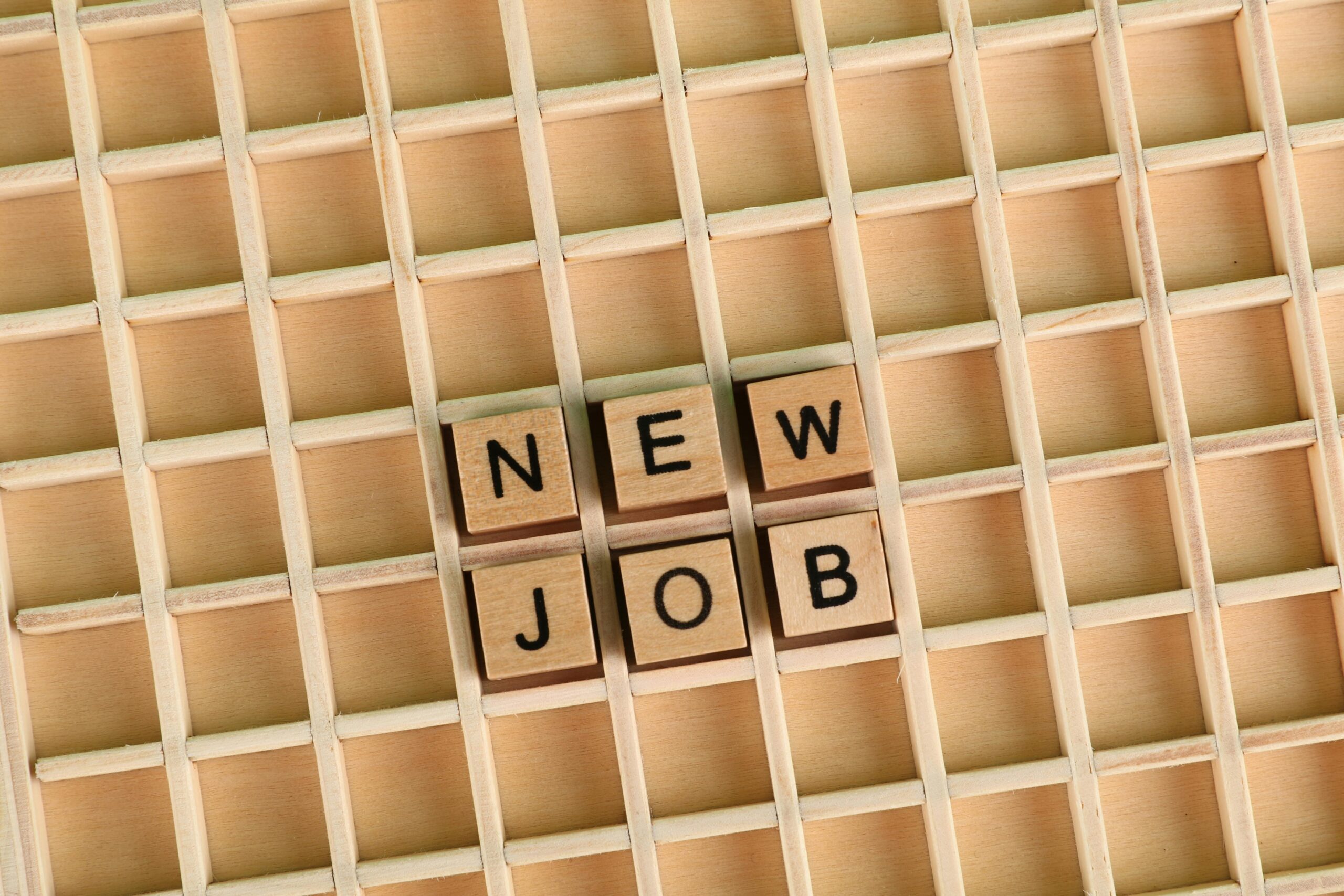 Discover the excitement of a new job with wooden letter tiles spelling 'NEW JOB' on a grid.