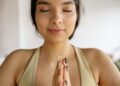 A peaceful woman meditating with closed eyes in a yoga pose, embracing mindfulness indoors.