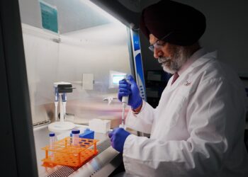 Scientist in lab coat using pipette in sterile lab. Focused research work in laboratory setting.