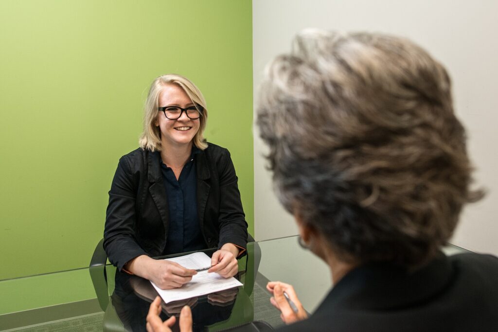 A smiling young woman sits across from a mature woman during a job interview, illustrating hiring for Audi's US factory.
