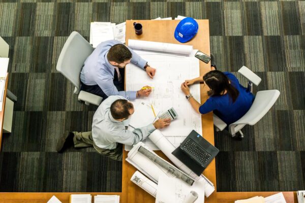 Architects and colleagues reviewing blueprints around a table, illustrating a rethink of project management.