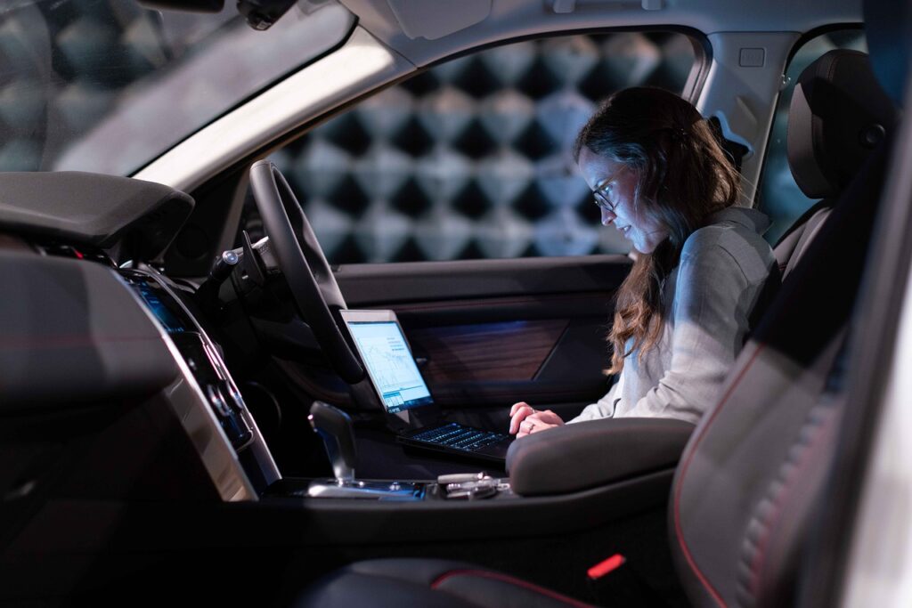 An engineer testing a car in an anechoic chamber with a laptop, illustrating AI-driven product development.